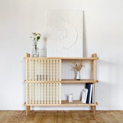 minimalistisches rega - design regal - japandi möbel - Blick in einen im Japandi-Stil eingerichteten Raum auf ein Regal aus Esche Massivholz mit Schiebeblenden aus Holz inszeniert vor weißer Wand mit Büchern und Vasen mit Blumen, einem Curious Penguin aus Porzellan und einem Gemälde